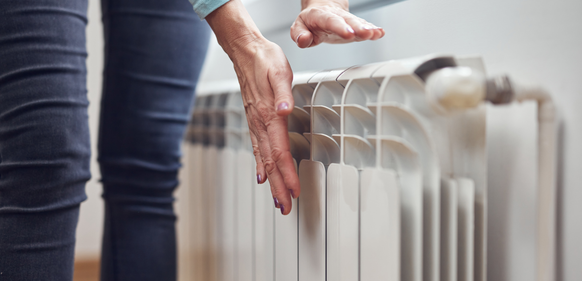 Woman heating her hands on the radiator during cold winter days.